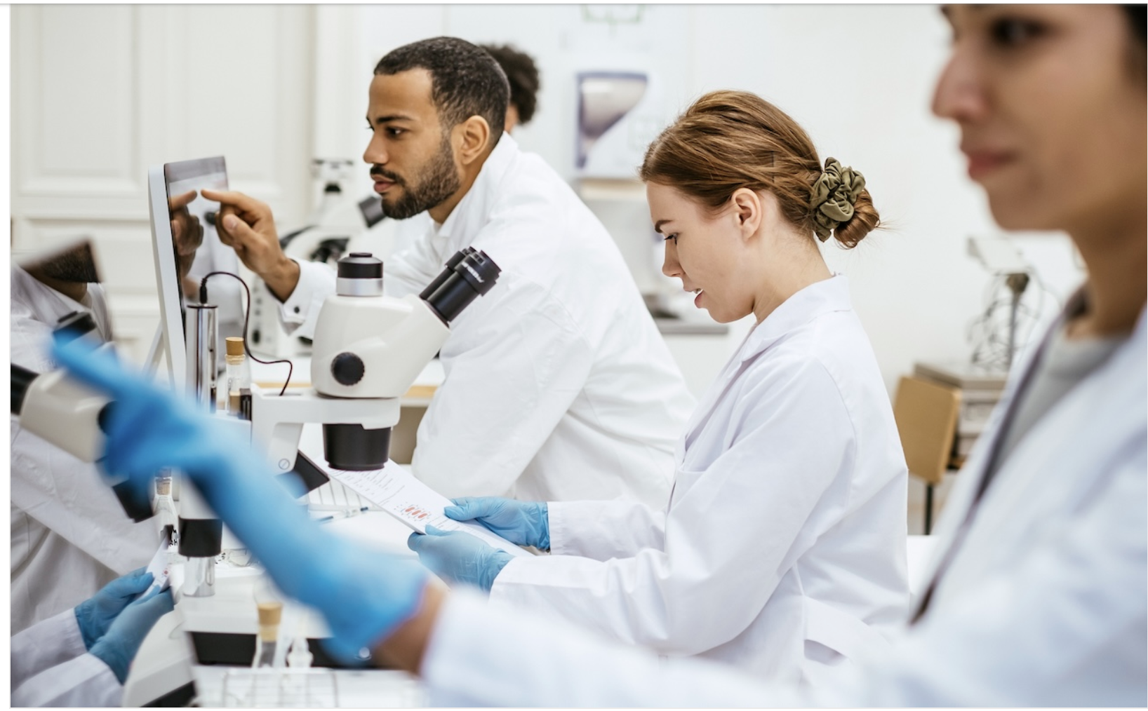 Diverse scientists in lab coats intently work with lab equipment and computers.