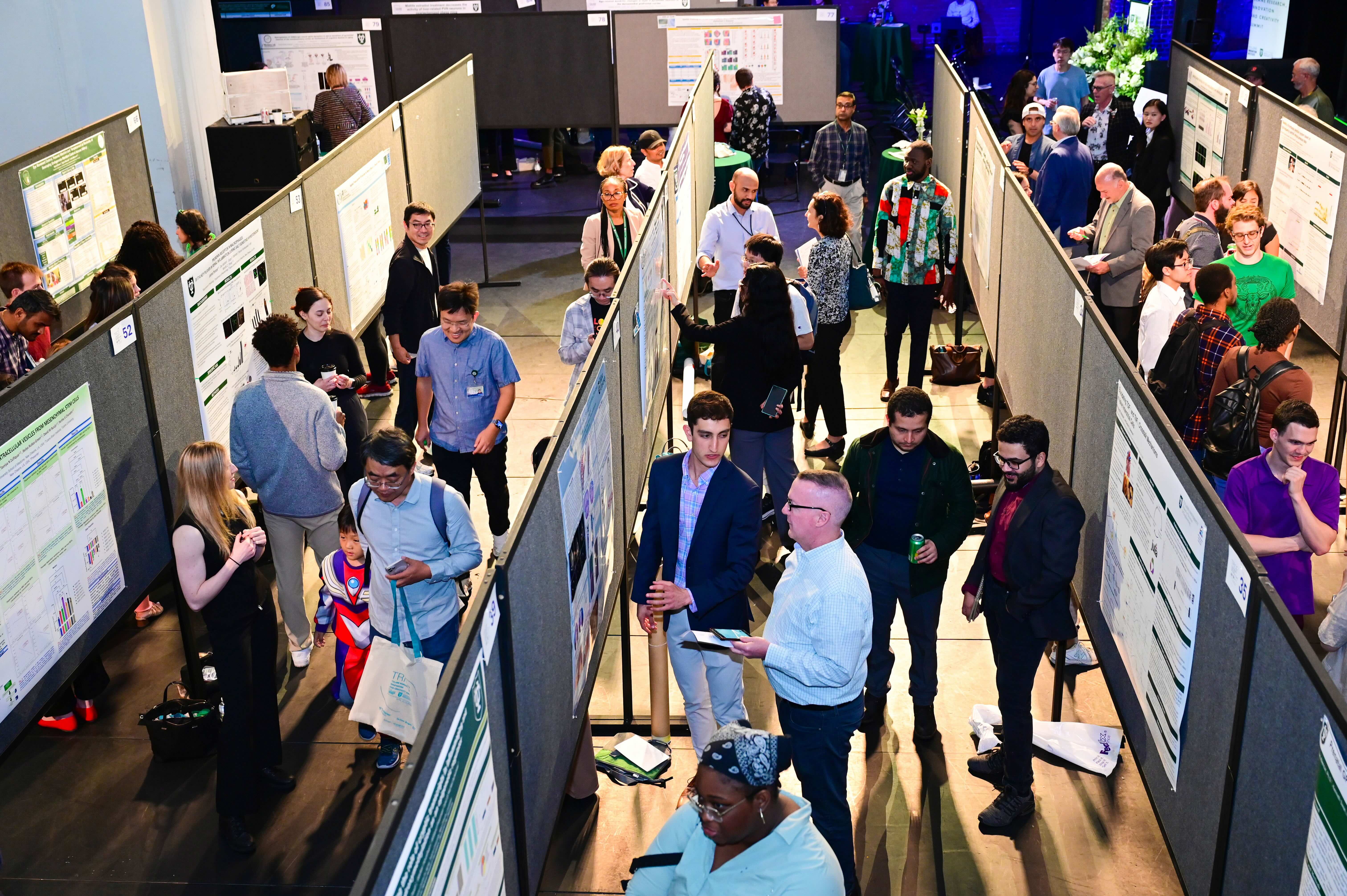 Busy academic poster session with many people viewing research posters on display boards.