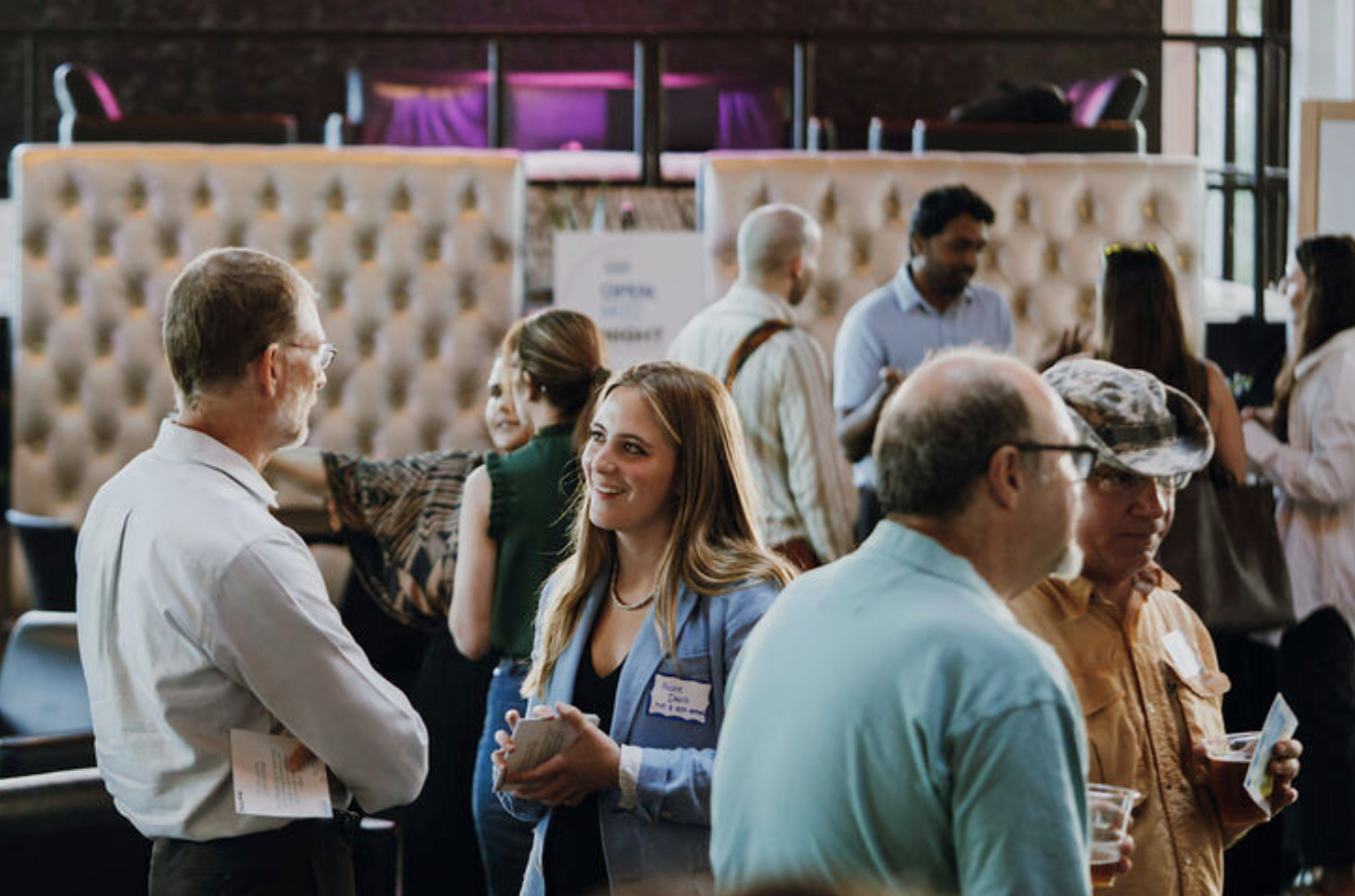 Photograph: People networking at an event, a smiling woman chats with a man.