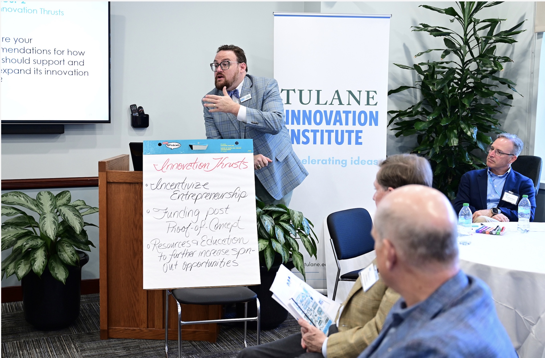 Man in suit speaks at a podium to an audience, Tulane Innovation Institute banner behind him. Casey Candebat