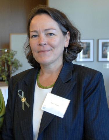Woman in dark blazer with green ribbon and name tag.